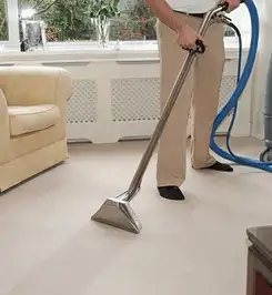 Professional carpet cleaner using a hot-water extraction wand and hose machine in a living room in Sarasota, FL.