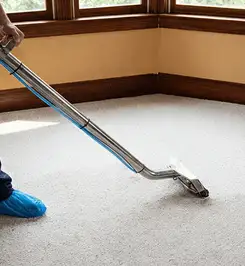Steam carpet cleaning technician using a hot-water extraction wand on a residential carpet, wearing blue protective shoe covers Sarasota, FL.