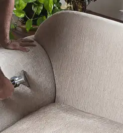 Professional upholstery cleaner deep-cleaning a fabric sofa with a handheld extraction tool and hose Sarasota, FL.