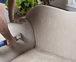 Professional upholstery cleaner deep-cleaning a fabric sofa with a handheld extraction tool and hose in Sarasota, FL.